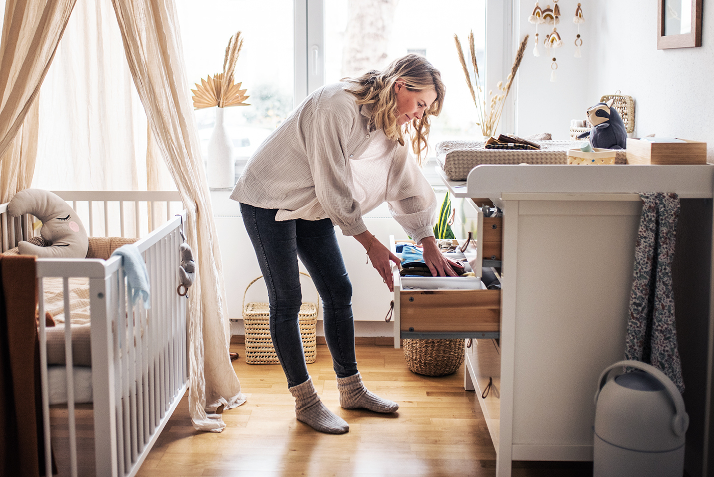 Junge Mutter verstaut Dinge in den Schubladen einer Wickelkommode