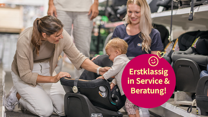 Erstklassig in Service & Beratung! Verkäuferin mit Kindersitz auf dem Boden. Daneben eine Mutter mit ihrer Tochter.