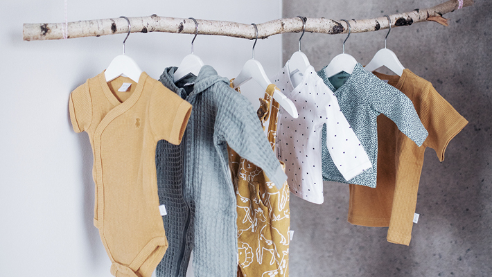 Babymode hängt mit Bügeln an einer Kleiderstange aus einem Birkenast