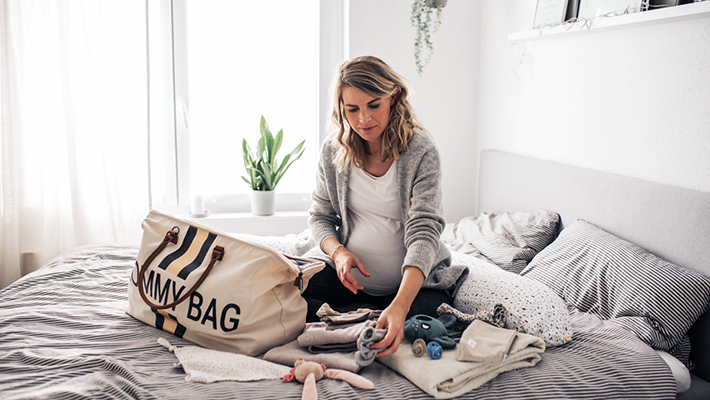 Schwangere Frau packt ihre Kliniktasche auf dem Bett